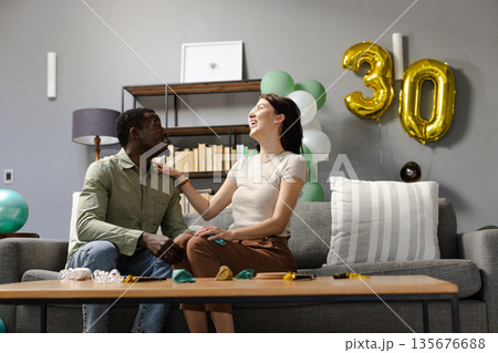 Couple celebrating 30th birthday at home, smiling and enjoying festive balloons Couple celebrating 30th birthday at home, smiling and enjoying festive balloons 135676688