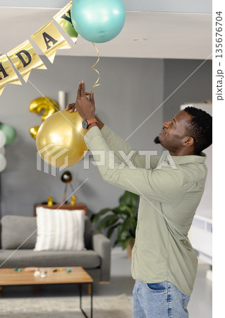 Man decorating living room with balloons for birthday celebration at home 135676704