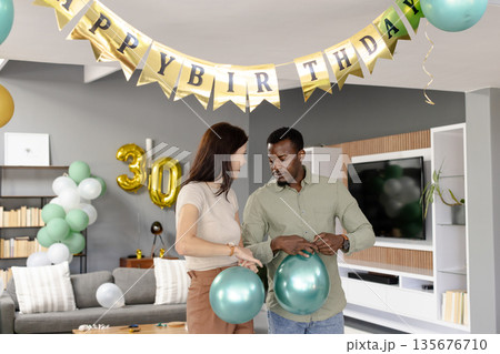 Couple decorating living room with balloons for birthday celebration at home 135676710