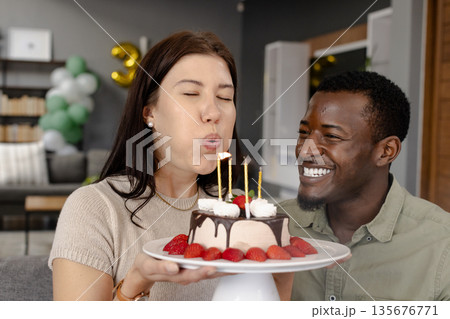 Blowing out candles, woman celebrating birthday with friend smiling at home 135676771
