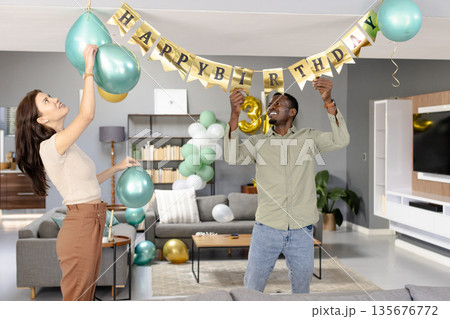 Friends decorating living room with balloons and banner for birthday celebration 135676772