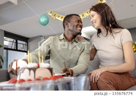 Couple celebrating birthday at home, smiling and enjoying cake together Couple celebrating birthday at home, smiling and enjoying cake together 135676774
