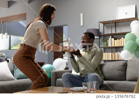 Woman presenting birthday cake to smiling man in living room celebration Woman presenting birthday cake to smiling man in living room celebration 135676782
