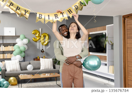 Decorating living room with birthday banner, couple celebrating special occasion together Decorating living room with birthday banner, couple celebrating special occasion together 135676784