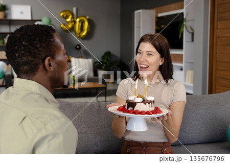 Woman holding birthday cake with candles, smiling at man in living room 135676796