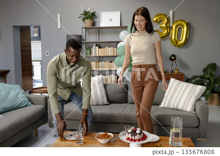 African American man and woman arranging cake and snacks for birthday celebration 135676808