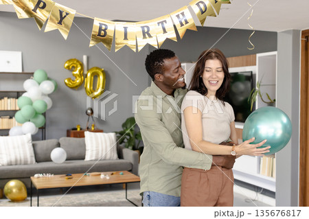 Couple celebrating birthday at home, holding balloons and smiling joyfully 135676817