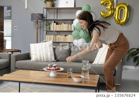 Woman arranging cupcakes on table for birthday celebration at home, smiling happily 135676824