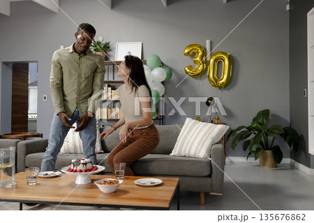 Celebrating 30th birthday, friends enjoying cake and snacks in modern living room 135676862