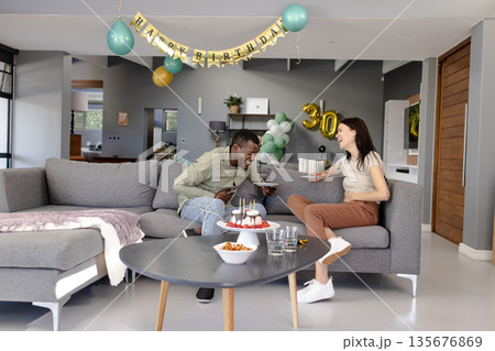 Friends laughing and enjoying birthday cake in modern living room celebration Friends laughing and enjoying birthday cake in modern living room celebration 135676869