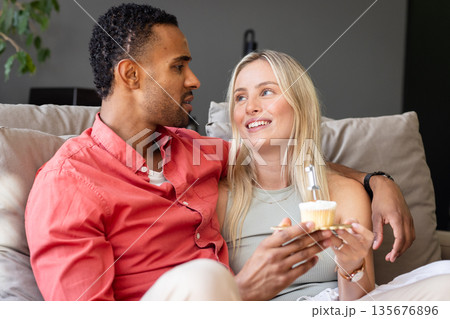 Couple sitting on couch enjoying cupcakes, sharing joyful conversation at home Couple sitting on couch enjoying cupcakes, sharing joyful conversation at home 135676896