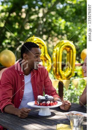 Man celebrating birthday outdoors with cake and balloons, smiling and chatting 135676897