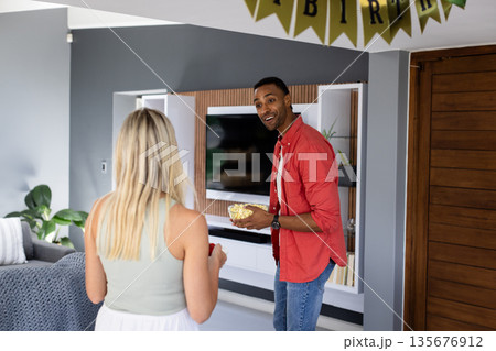 Holding popcorn, African American man smiling at woman during birthday celebration at home Holding popcorn, African American man smiling at woman during birthday celebration at home 135676912