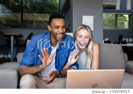 Happy couple video chatting on laptop at home, waving and smiling warmly Happy couple video chatting on laptop at home, waving and smiling warmly 135676917