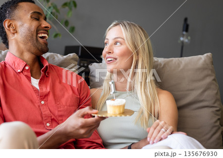 Couple laughing and enjoying cupcake together on cozy couch at home Couple laughing and enjoying cupcake together on cozy couch at home 135676930