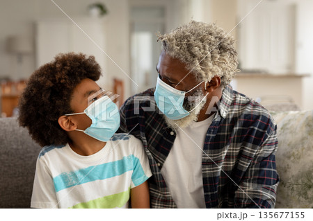 Boy and senior man wearing face mask looking at each other at home Boy and senior man wearing face mask looking at each other at home 135677155