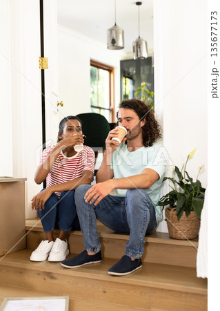 Young diverse couple sitting on stairs, enjoying coffee together at home, relaxing 135677173