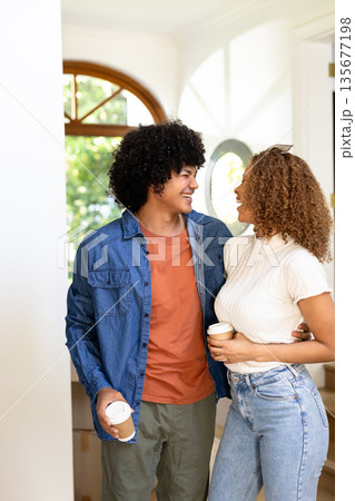 Young diverse couple enjoying coffee together, smiling and embracing in cozy home setting 135677198