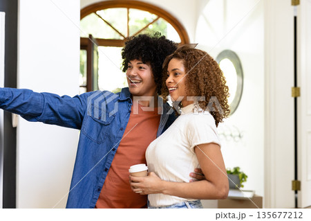 Young couple smiling and pointing while enjoying coffee at home together Young couple smiling and pointing while enjoying coffee at home together 135677212