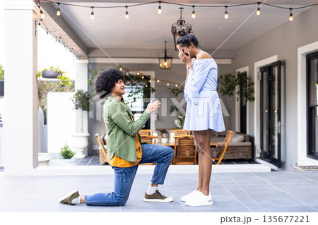 Young man proposing to surprised woman on patio, creating romantic moment 135677221