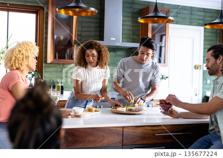 Young friends preparing meal together in modern kitchen, enjoying cooking experience 135677224