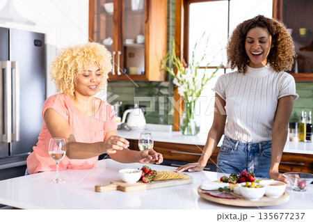 In kitchen, friends sharing laughter and conversation while enjoying wine and snacks In kitchen, friends sharing laughter and conversation while enjoying wine and snacks 135677237