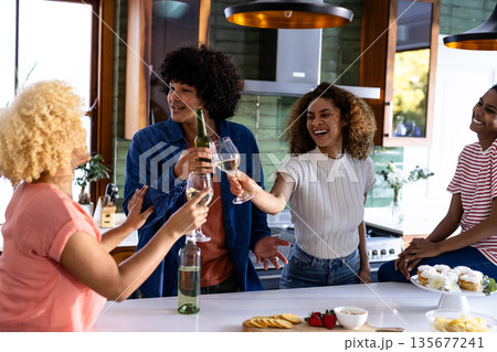 Diverse friends toasting with drinks in modern kitchen, enjoying celebration together 135677241