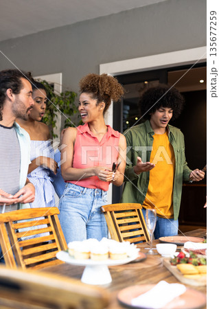 Young Diverse friends enjoying conversation and laughter around dining table with cupcakes Young Diverse friends enjoying conversation and laughter around dining table with cupcakes 135677259