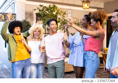 Young Diverse friends celebrating outdoors, raising glasses and enjoying joyful gathering 135677264