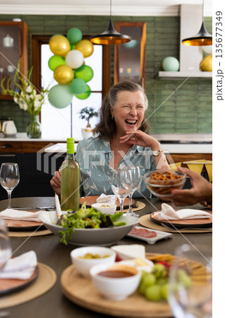 At dining table during party, senior woman laughing joyfully with friends At dining table during party, senior woman laughing joyfully with friends 135677349