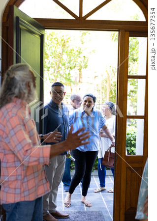 Welcoming friends, diverse senior group having cheerful conversation at home doorway Welcoming friends, diverse senior group having cheerful conversation at home doorway 135677354