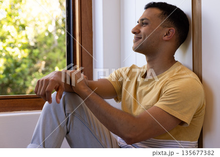 Young man sitting by window, enjoying peaceful moment at home Young man sitting by window, enjoying peaceful moment at home 135677382