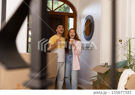 Young couple excitedly entering new home surrounded by moving boxes and plants 135677385