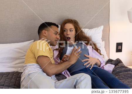 Young couple on bed excitedly looking at ultrasound photo, expecting baby 135677395