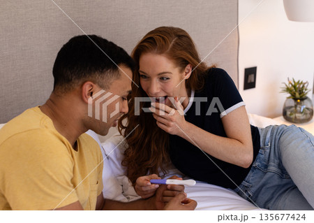 Young couple on bed joyfully reacting to positive pregnancy test result 135677424