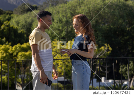 Holding smartphone and conversing, couple outdoors surrounded by nature 135677425