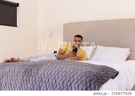 Relaxing on bed, young man using smartphone and smiling at home 135677426