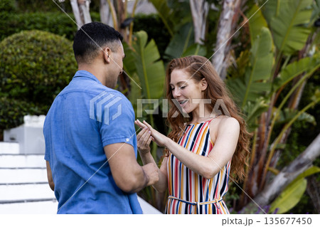 Young couple in garden, woman excitedly looking at ring on her finger Young couple in garden, woman excitedly looking at ring on her finger 135677450