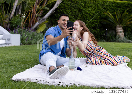 Sitting on picnic blanket, couple taking selfie with smartphone, smiling happily Sitting on picnic blanket, couple taking selfie with smartphone, smiling happily 135677483