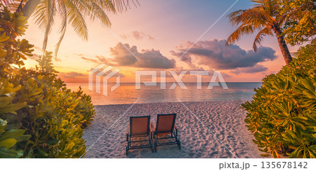Romantic sunset at tropical beach with palm leaves, chairs and ocean view, panoramic landscape with amazing sky and clouds, perfect for travel, vacation, and lifestyle background 135678142
