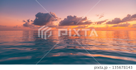 Amazing panoramic ocean sunset with calm water surface, colorful romantic sky, clouds and tranquil horizon creating a meditative tropical nature background for travel, wellness, and lifestyle design 135678143