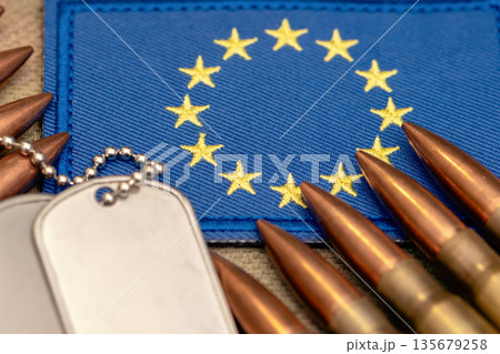 Military ammunition and metal identification tags on blue European Union flag. 135679258