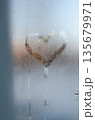 A heart-shaped clear patch melted into frosty glass, glowing warmly against cold blue condensation. 135679971
