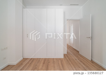 A bright, minimalist interior featuring a white wardrobe and wooden flooring. The walls are plain and the space is uncluttered, emphasizing simplicity and modern design. A bright, minimalist interior featuring a white wardrobe and wooden flooring. The walls are plain and the space is uncluttered, emphasizing simplicity and modern design. 135680127