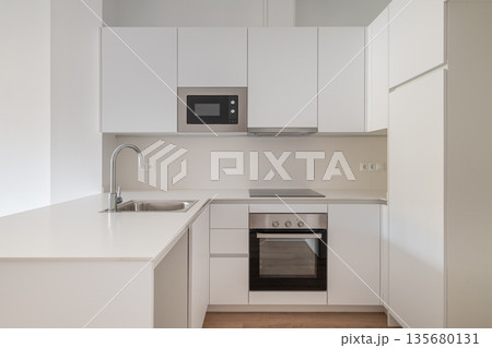 Modern kitchen with white cabinets, stainless steel appliances, and a minimalist design. Features a sink, microwave, and oven. Modern kitchen with white cabinets, stainless steel appliances, and a minimalist design. Features a sink, microwave, and oven. 135680131