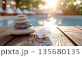 Smooth zen stones stacked on wooden deck by pool with white orchid, creating serene spa environment 135680135