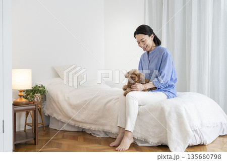 ベッドに座って愛犬を抱っこするミドル女性 135680798
