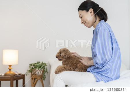 ベッドに座り膝の上の愛犬をなでるミドル女性 135680854