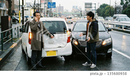雨の都会で発生した激しい追突事故 破損した車両を指差し保険会社へ電話する男性 物損トラブル 135680938