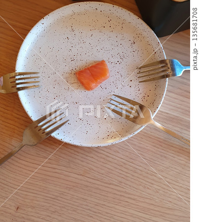 A small piece of red fish lies on a plate, and four forks are located around it. A stylish composition 135681708
